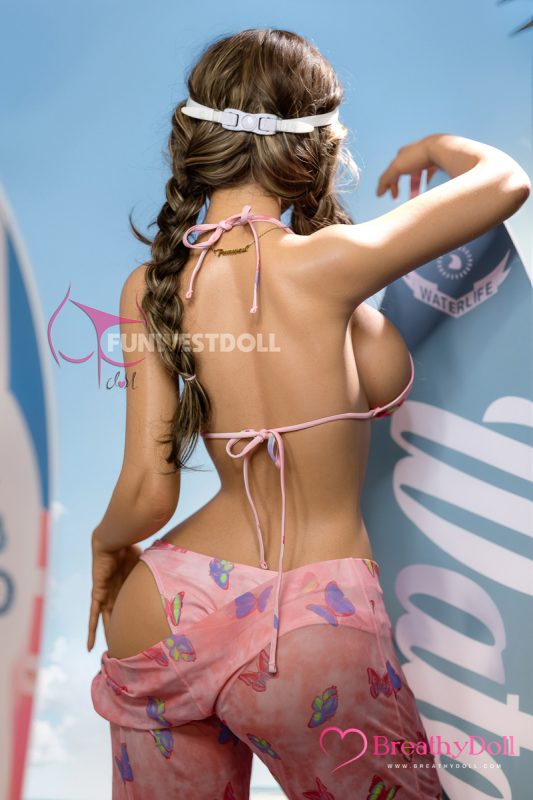Pink bikini top and butterfly-printed pants worn by a realistic companion doll with long, wavy brown hair styled in braids. She has a white headband and a gold necklace that spells "Dreamer".