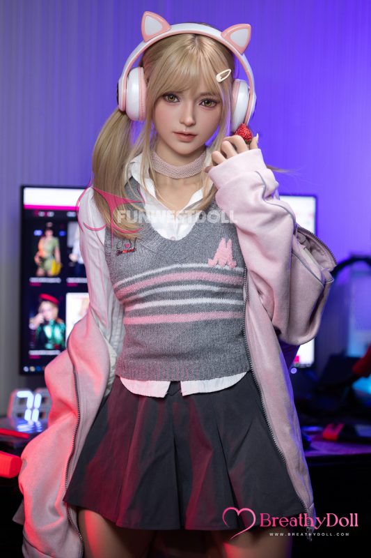 Soft-blonde female doll with realistic facial features, wearing pink cat-eared headphones, a gray and pink sweater vest, and a white shirt, holding a strawberry in a vibrant gaming room setting.