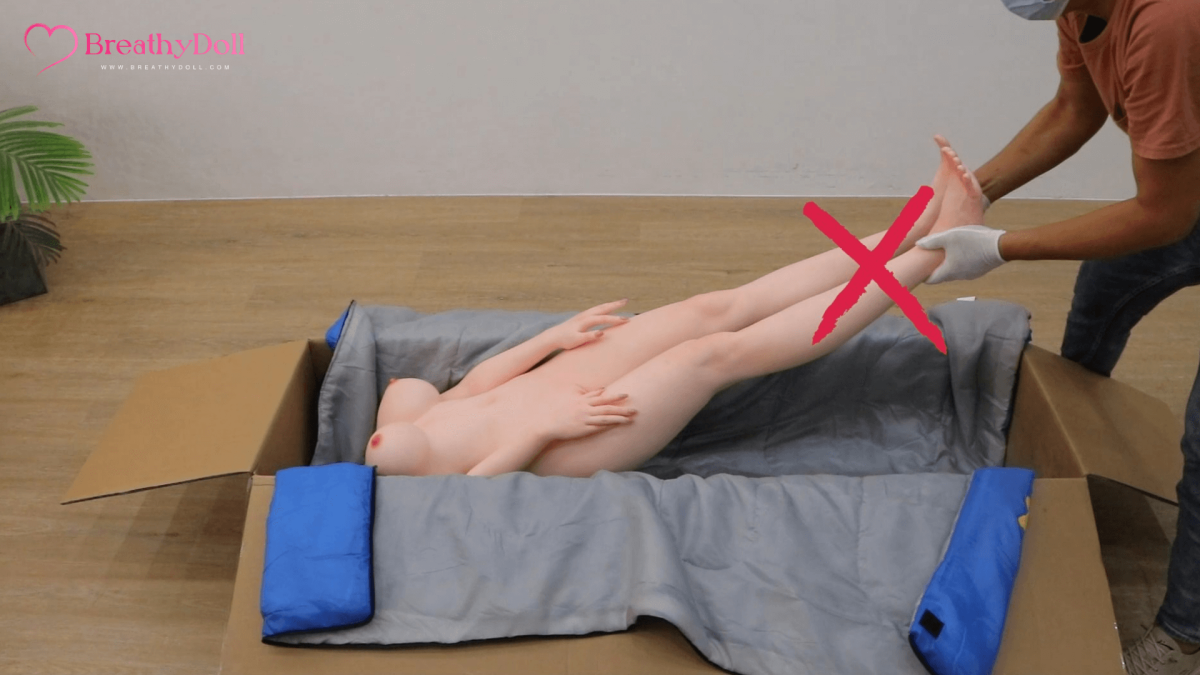Soft realistic companion doll lying on a padded surface, showcasing detailed facial features and natural skin tone, perfect for adult companionship; hand of a person handling the doll.