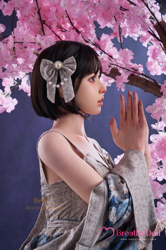 A realistic 153cm silicone companion doll named Lina, featuring a head ROS Max A3, with short black hair and a decorative bow, posed against pink cherry blossoms.