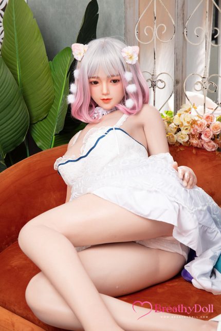 Realistic doll with pink and white hair, floral hair accessories, sitting on a sofa with green plants and flowers in the background.